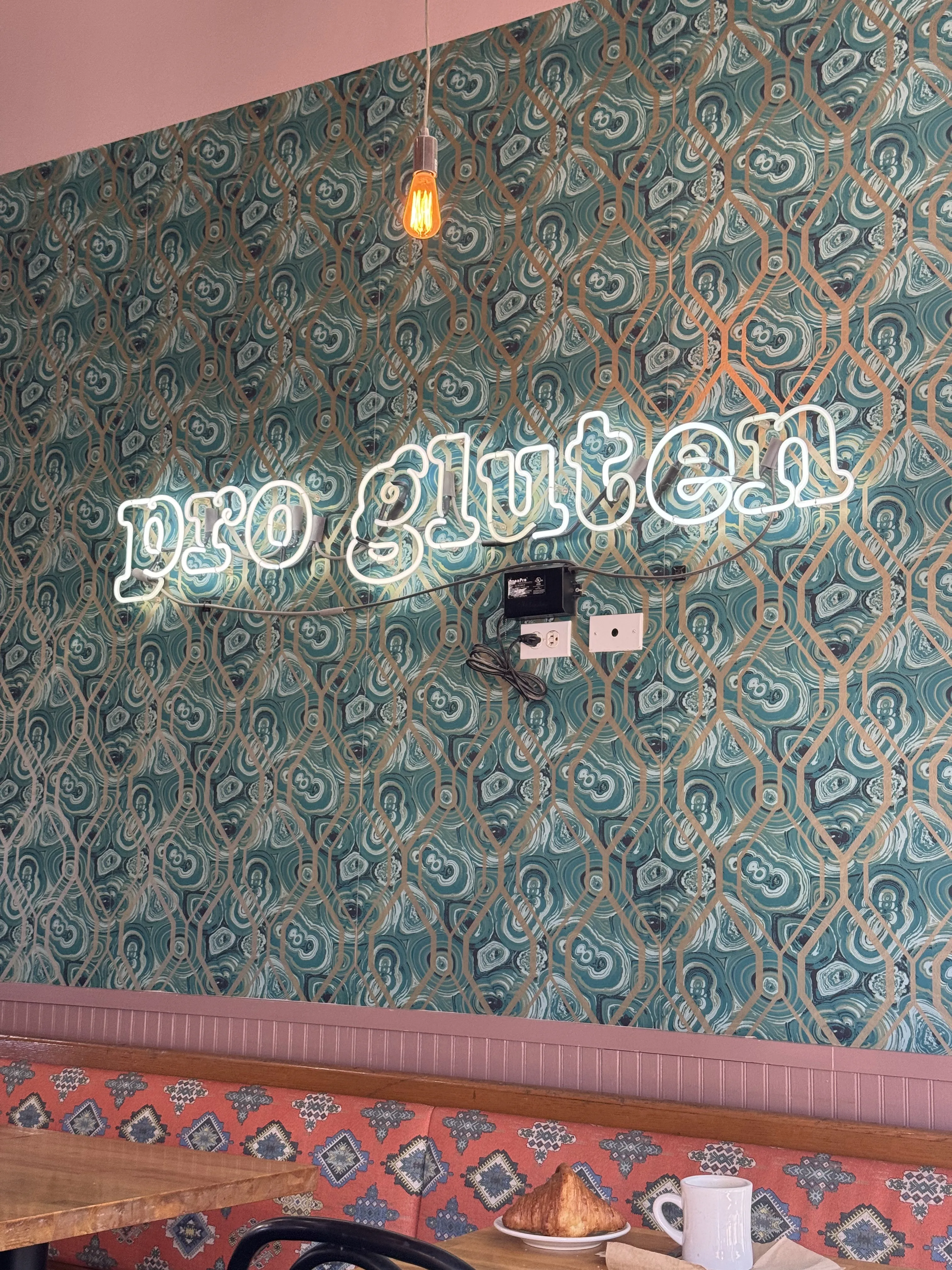 Neon sign on a wallpapered wall that reads "pro gluten"
