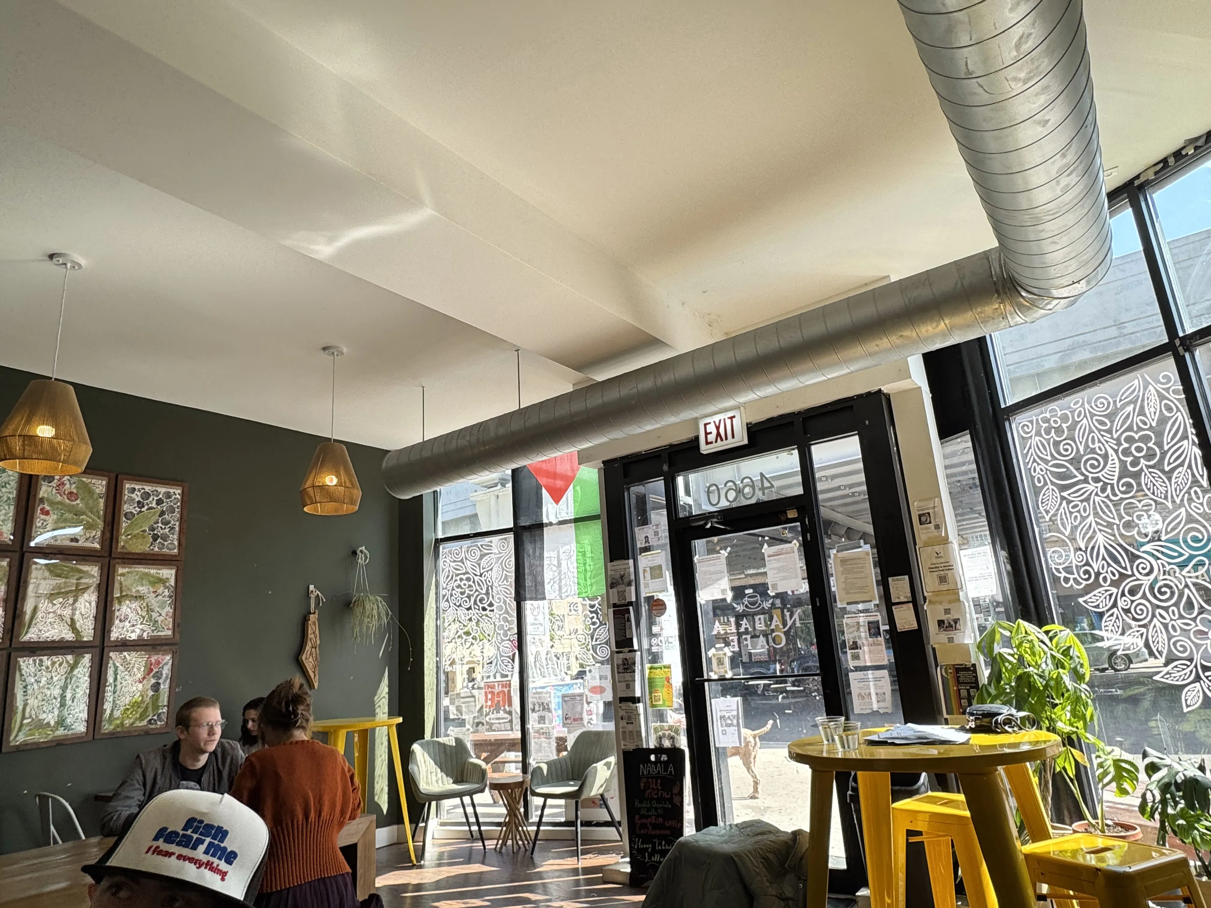 Full cafe view of Nabala cafe. Olive-painted wall on left, big windows elsewhere. Varied seating and tables. Palestinian flag in display