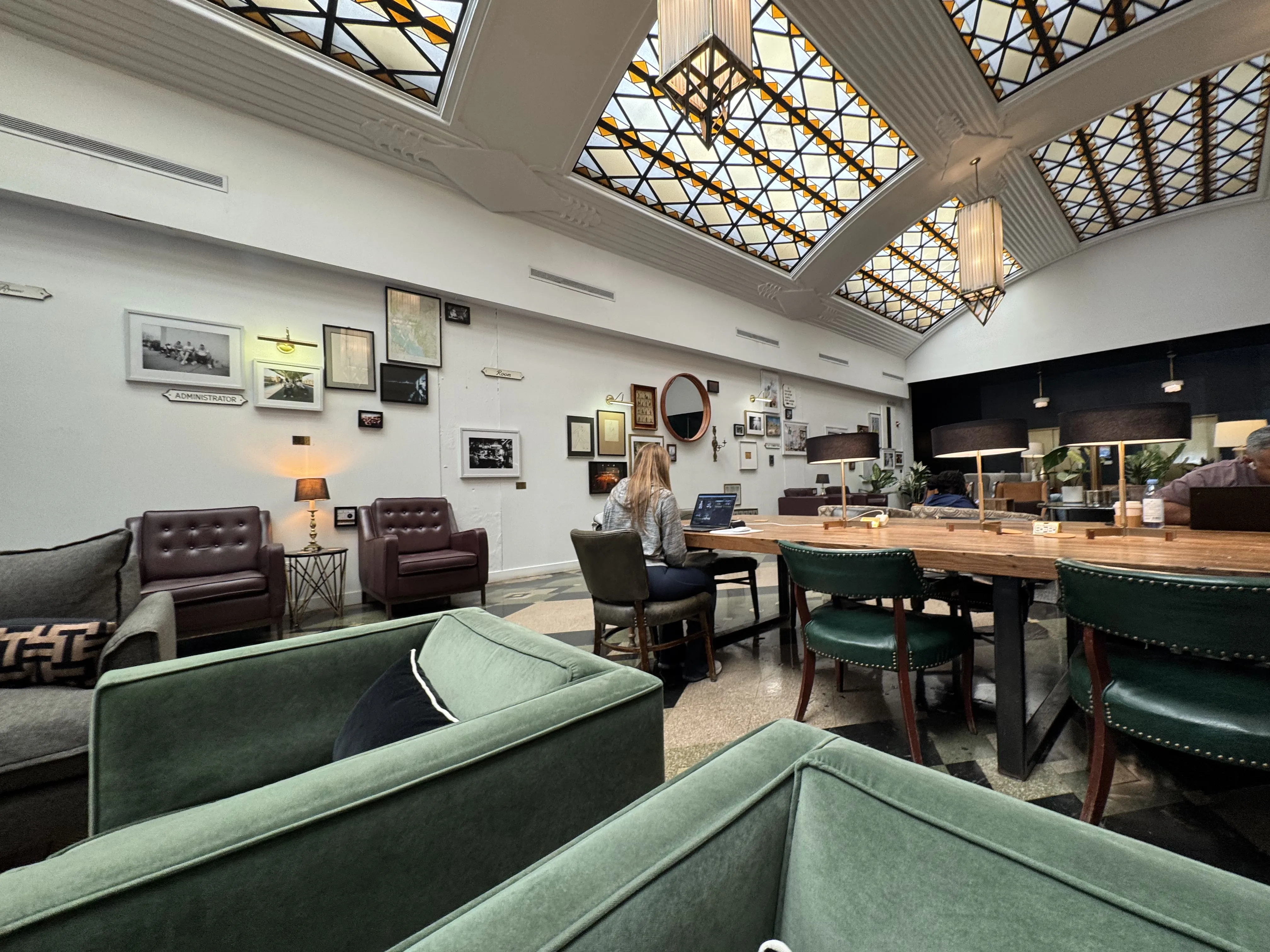 Large lobby type area with a series of armchairs and big work tables. Large curved old-school skylights above. An elevator bank in the back