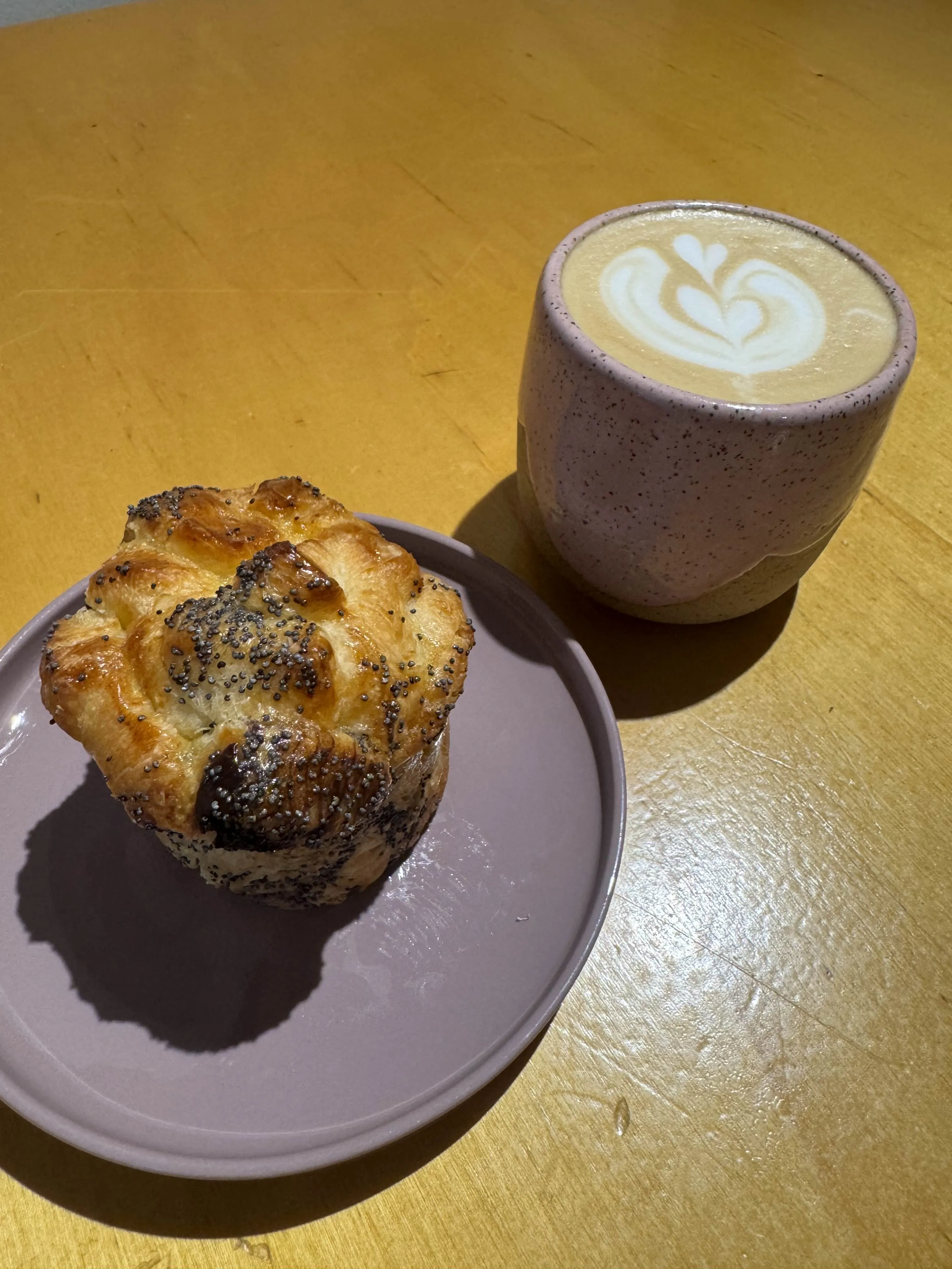 Cute ceramic cup with a latte next to a plate with a poppyseed muffin