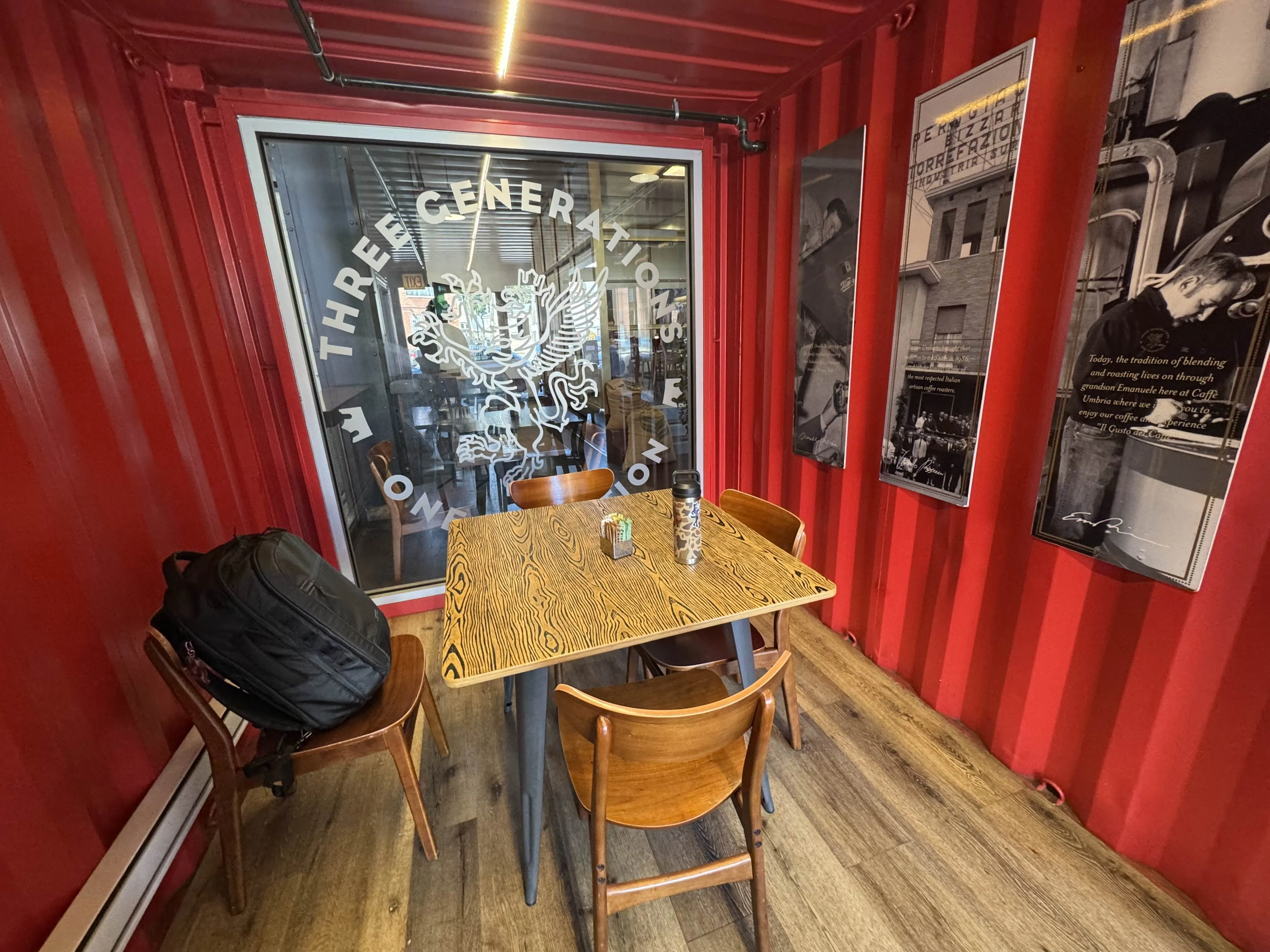 View of the immediate entrance of the cafe, which features the only large 4-person table there. It sits infront of a glass with vinyl decor of the cafe logo.