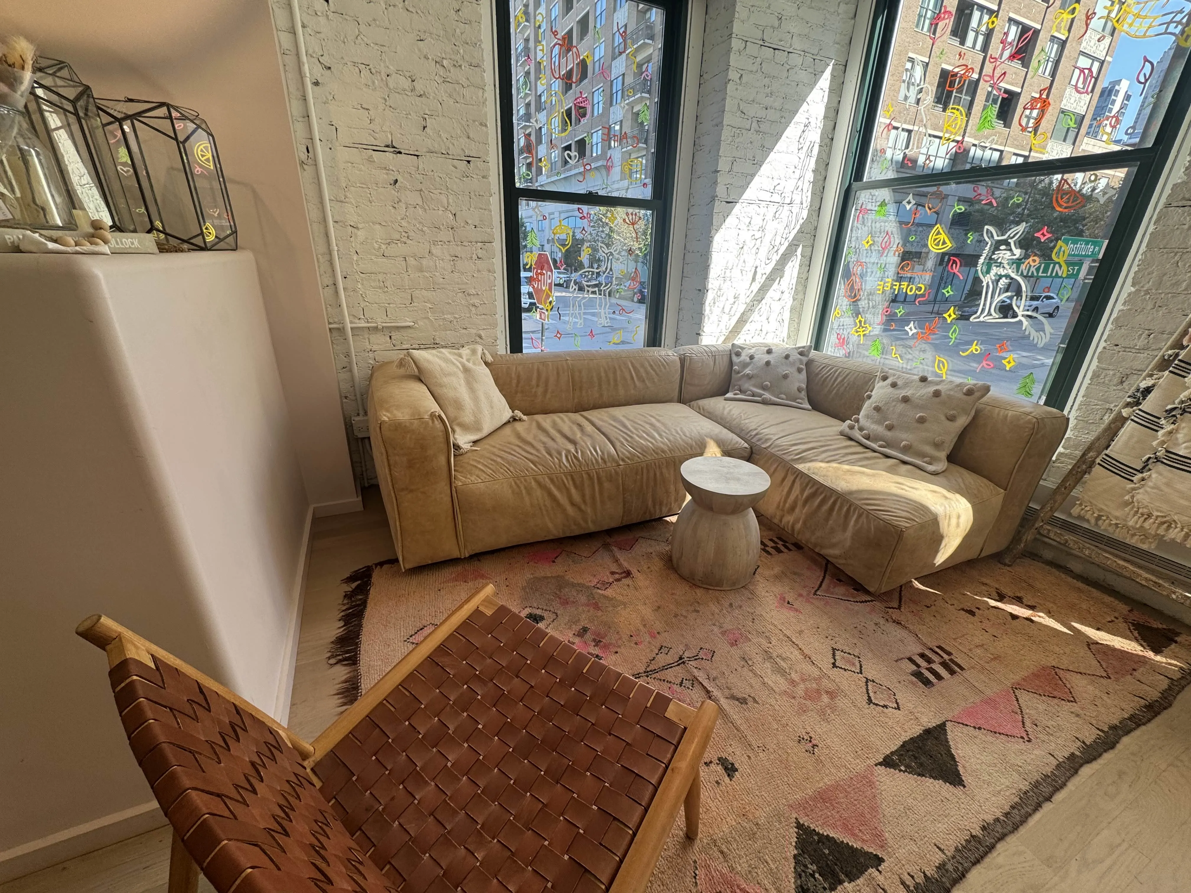 Cute L-shaped couch, small wooden table, and a woven faux-leather chair in a cute corner atop an incredibly old, ratty floor-rug