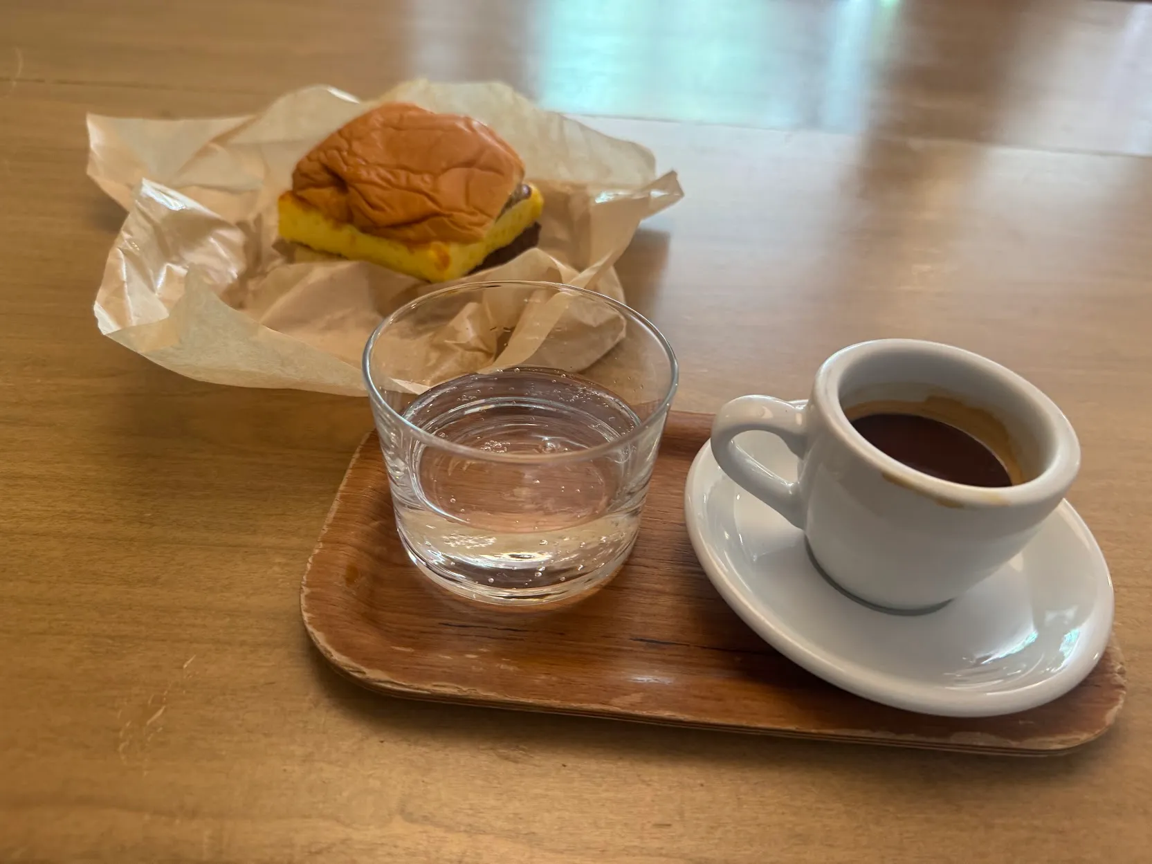 An espresso shot next to a glass of sparkling water. Behind is a breakfast sandwich with a square egg patty