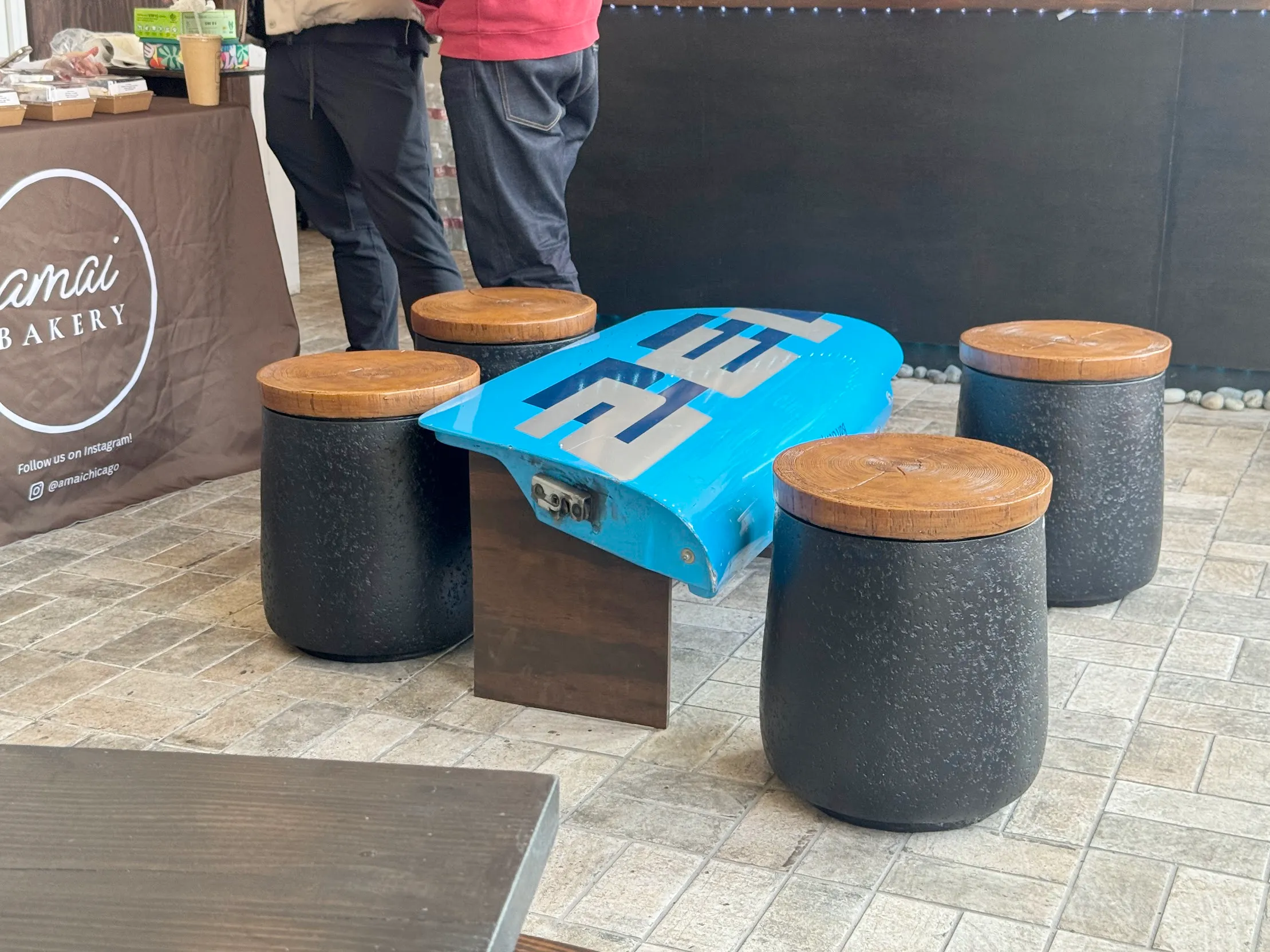 Focused photo of a blue car door built into a table stand with 4 black stools with wooden stool toppers