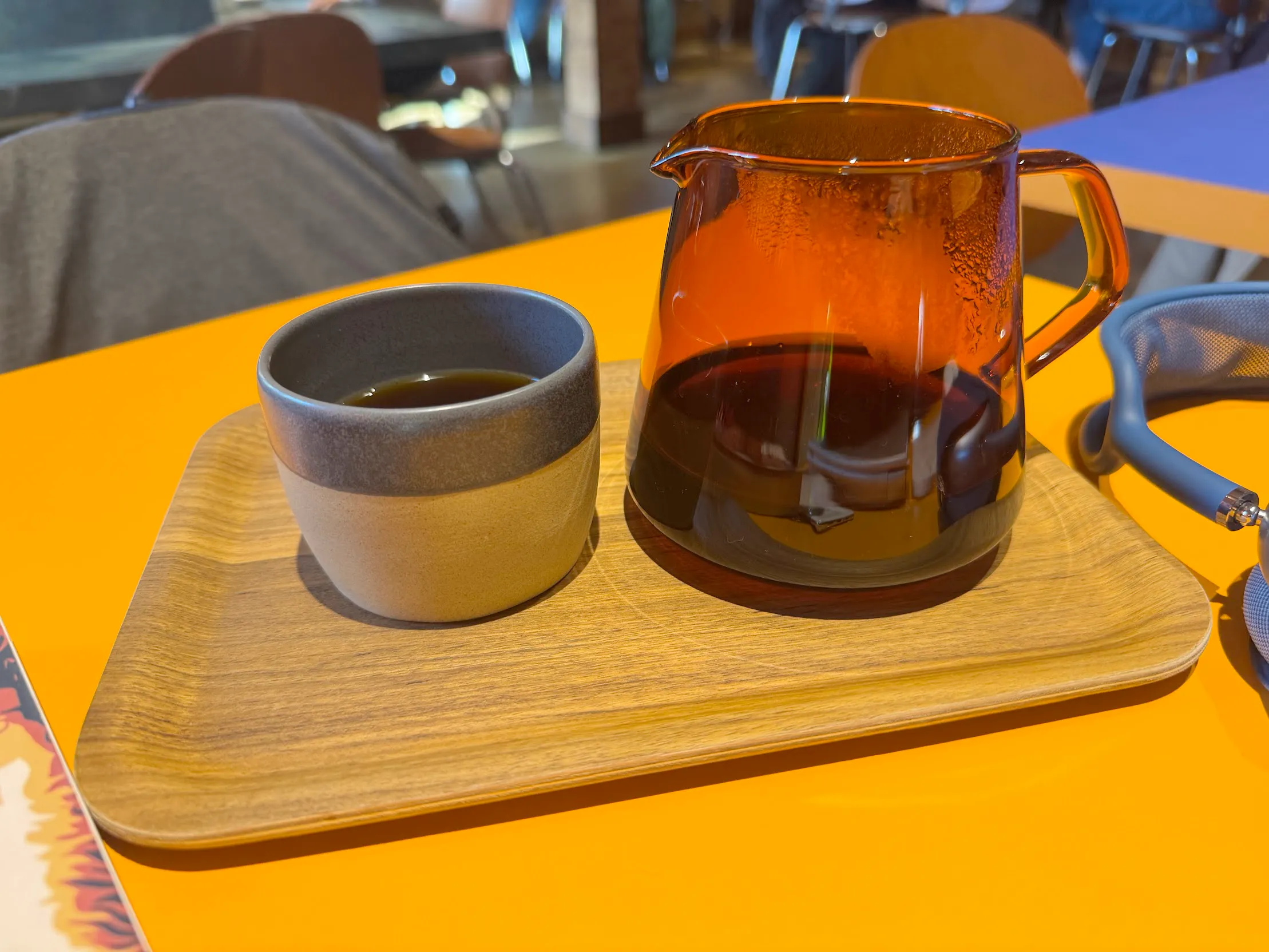 Pour-over setup on a wooden tray. The carafe is a deep orange/brown and the cup is a round stoneware cup w/o a handle. Wooden tray is sitting on an orange table-top