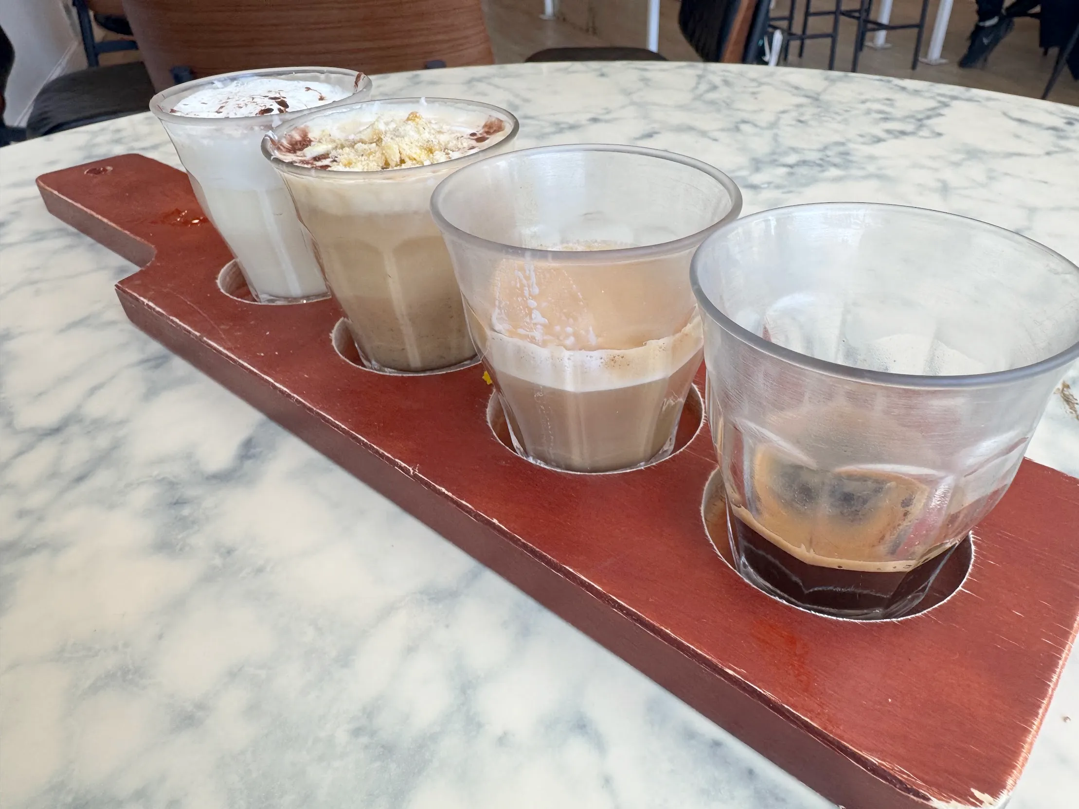 A "coffee flight". A serving board with 4 cortado-sized cups with 4 different coffee drinks, one of which is obviously espresso, the rest are a mix of foam and milk.