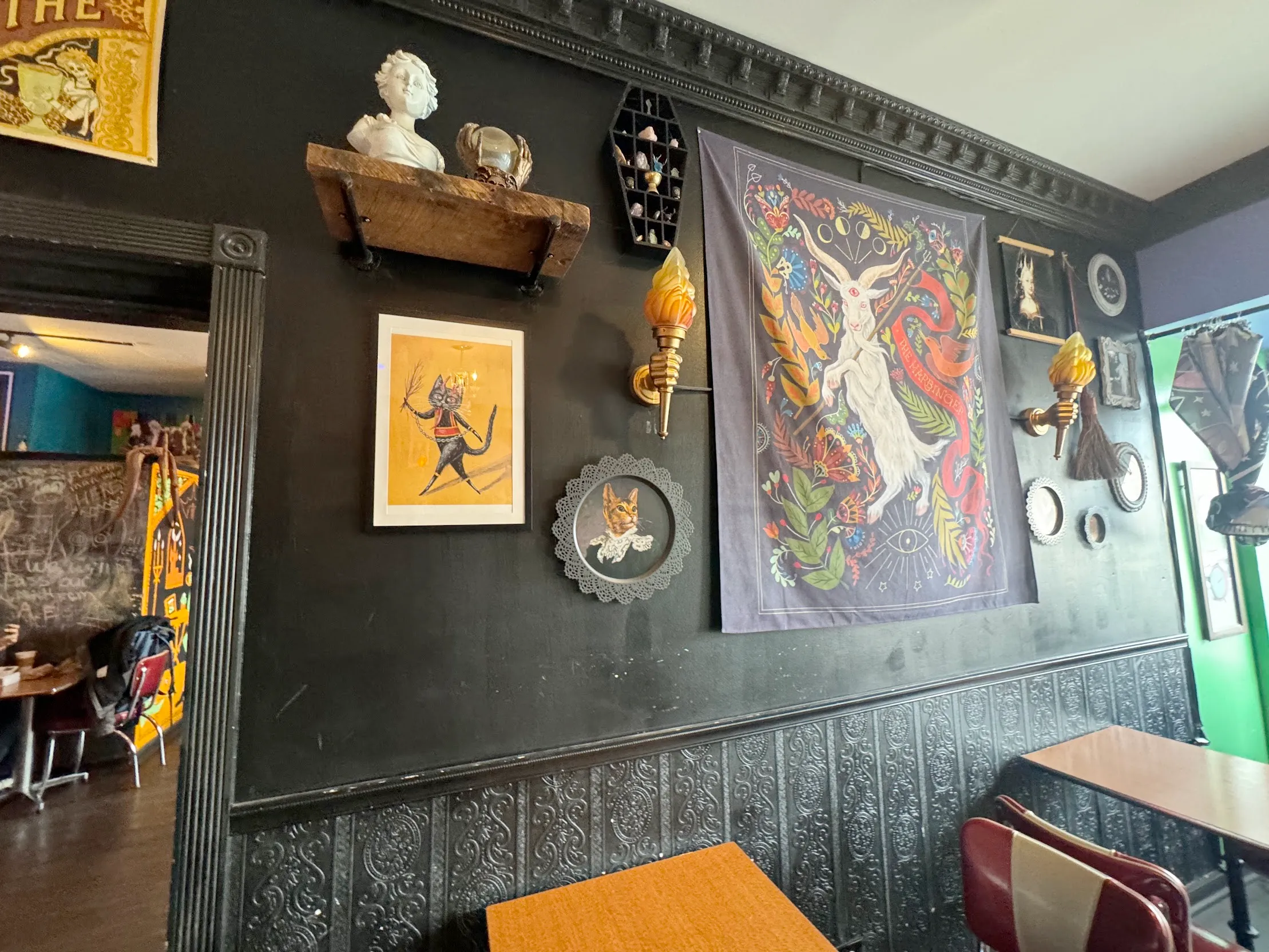 View of a black-painted wall covered in various tapestry and framed art. A doorway is visible to the left into more cafe space.