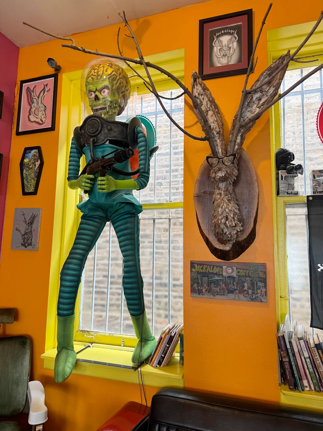 Orange wall with a prominent Jackalope bust next to a full-body Mars Attacks! alien figure braced against the window