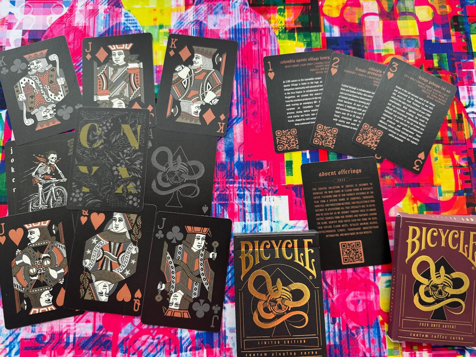 A series of black playing cards with custom ONyx coffee motifs and text atop a wildly bright pink and yellow glitch design desk mat