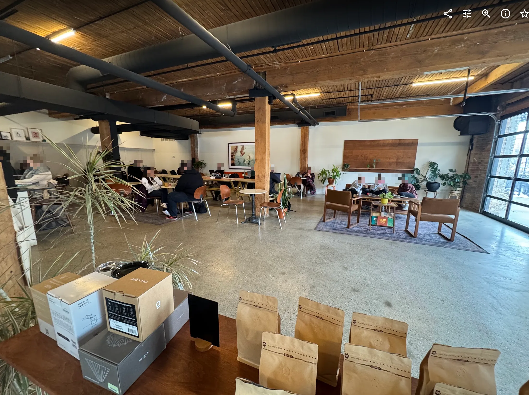 Full view of the cafe seating. Many people are dispersed among small 2-top tables and couch seating with tasteful art and dracaneas placed around.