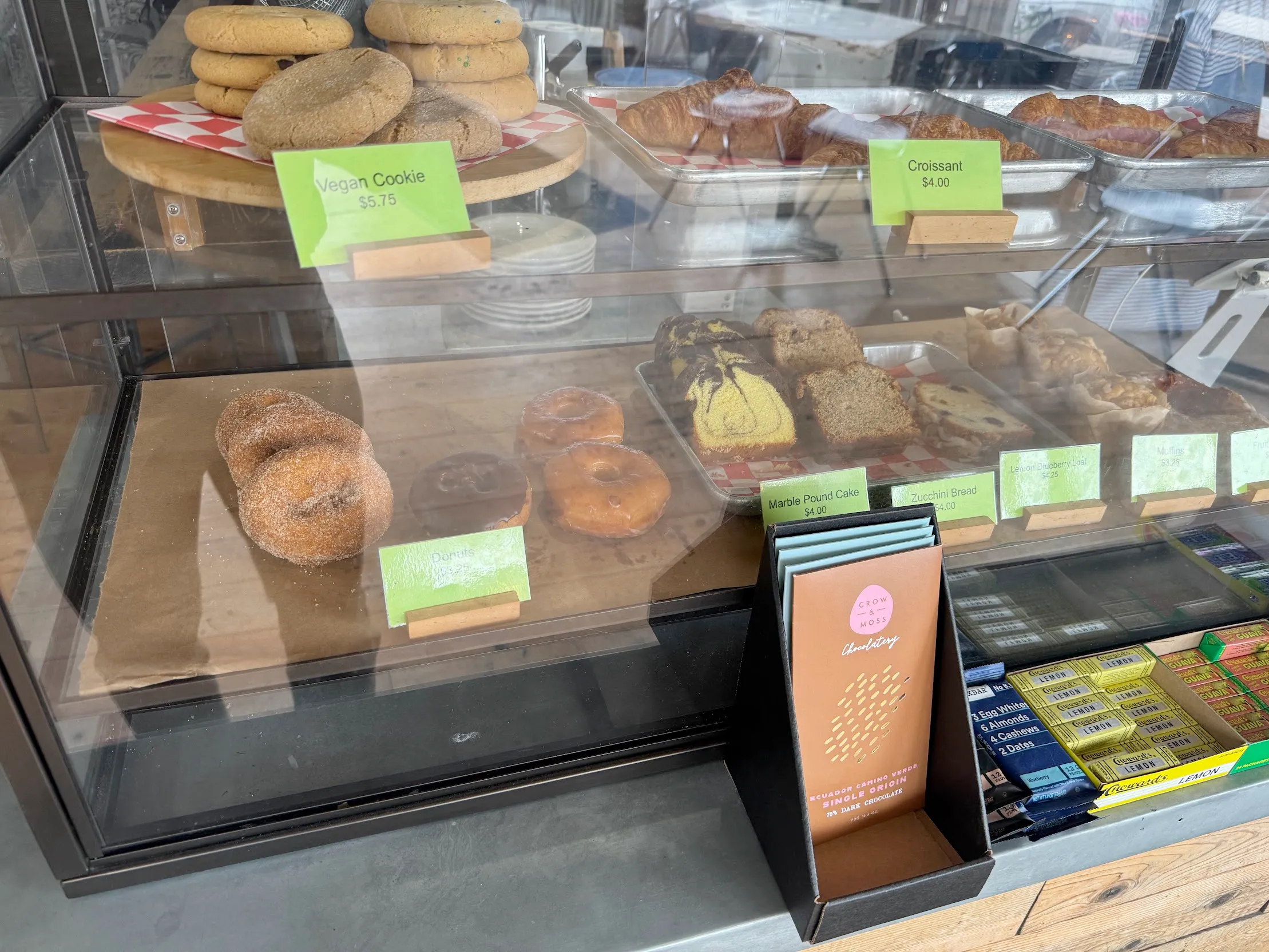 Amateur photo of a glass pastry container with excessive glare on the glass. Donuts and bread slice things inside next to lime green price placards