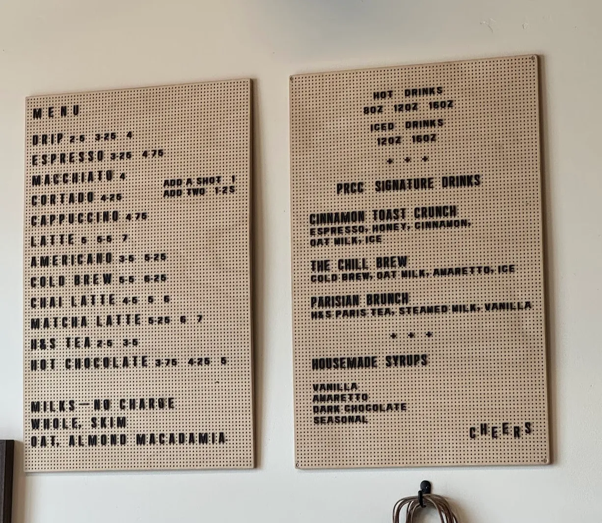 Menu and price list. Tan peg board with black letters atop white wall.