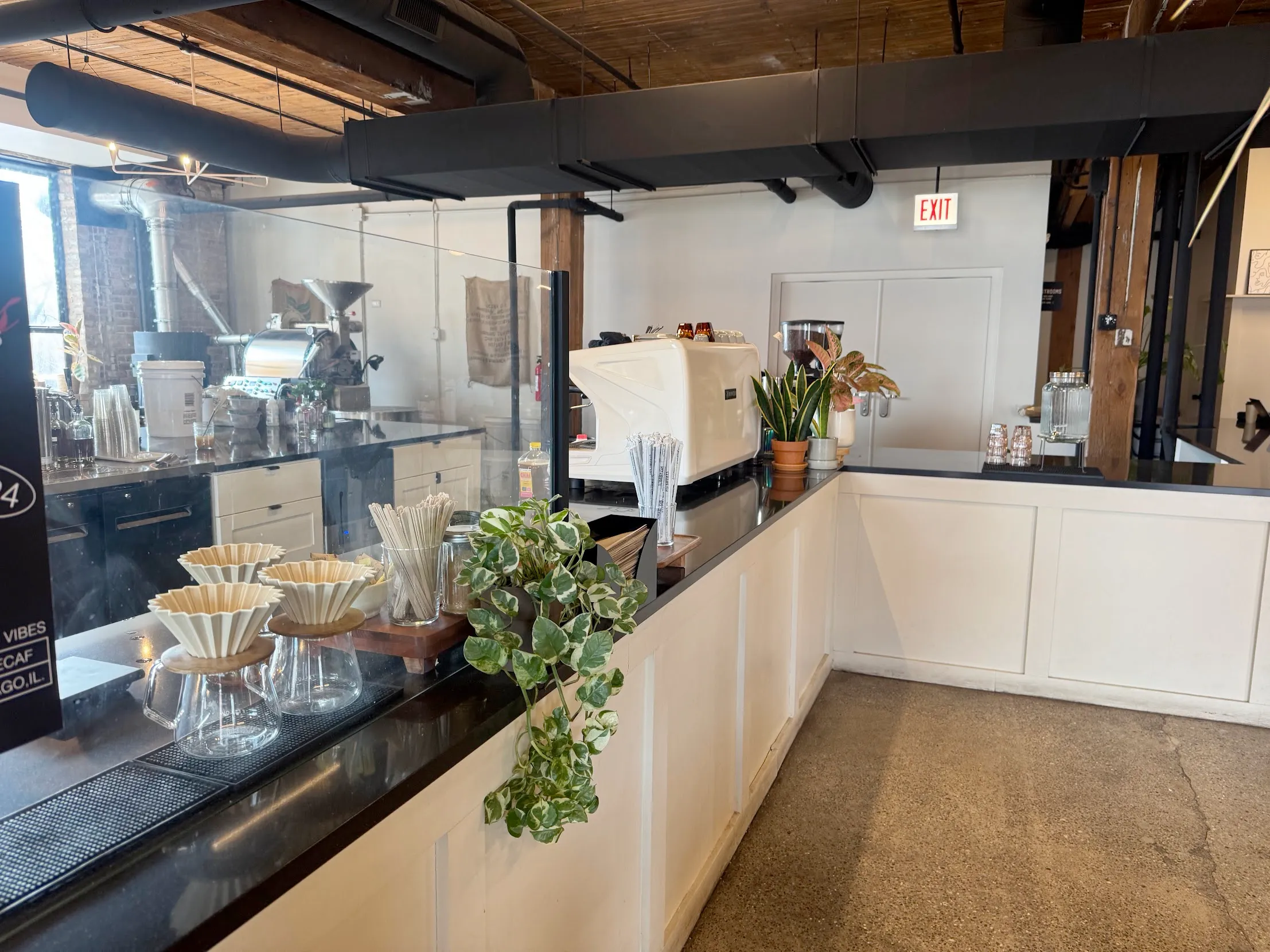 Close-angle of the coffee brewing and roasting area with no employees in sight. Image is dominated by the large espresso machine and the origami pour-over cones near the forefront.