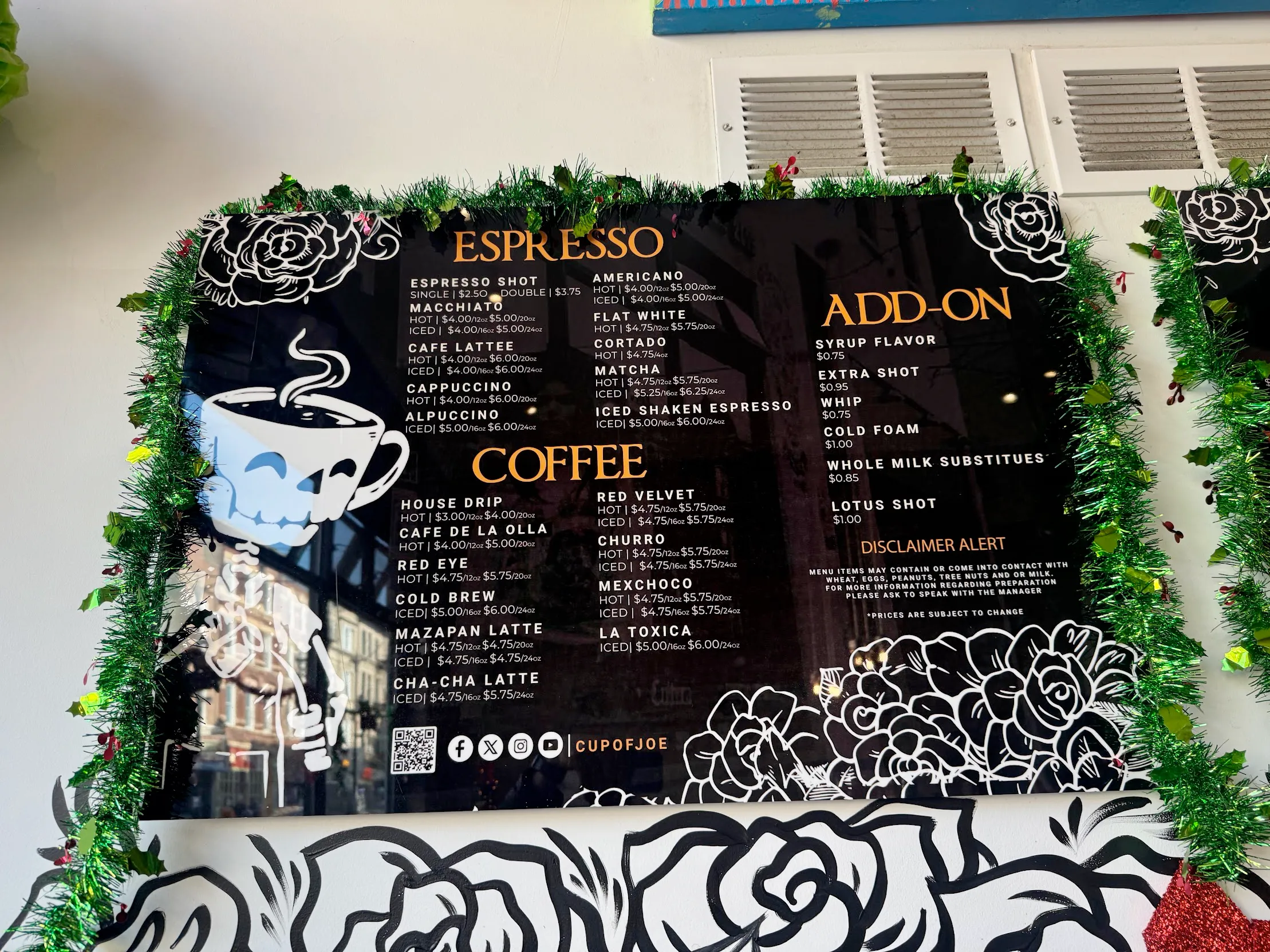 Photo of a glossy menu board, with the cafe's signature skeleton character (with steaming espresso cup head) pouring a cuppa