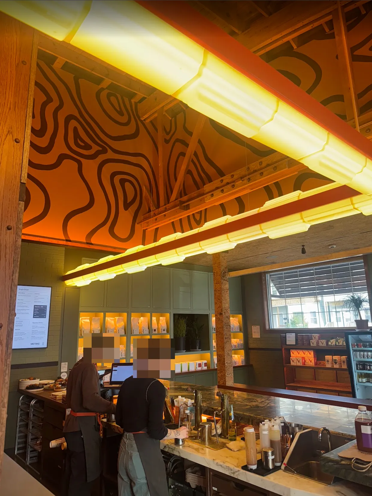 Angle of the espresso bar from the back, showcasing the lights and ceiling/wall decorations. The queue is currently empty, and you can see the window out to the street along side the merch wall