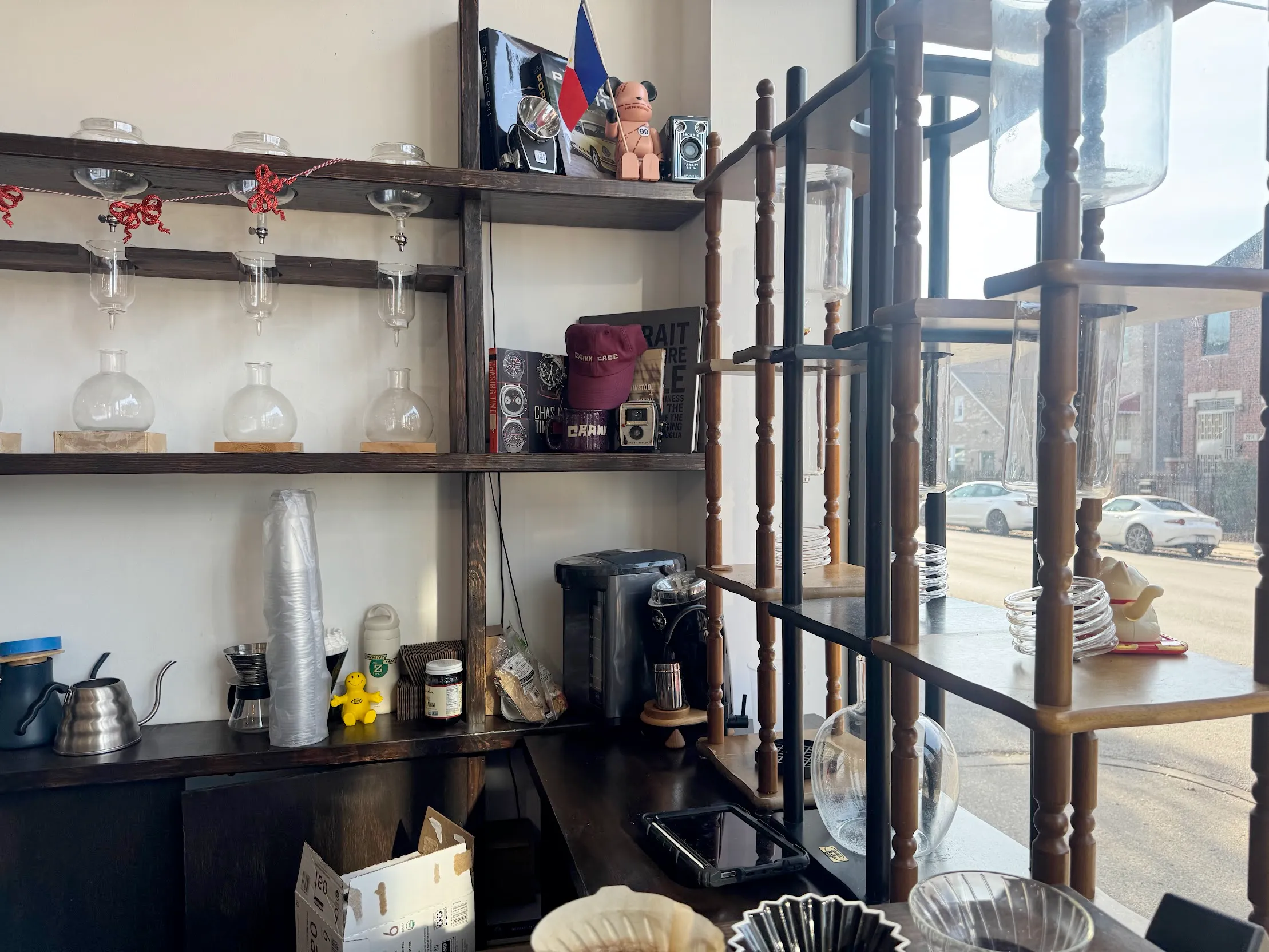 Photo of a variety of uncommon coffee brewing equipment, including 3 prominent cold-brew drip towers on the right. There is a pour-over station in the front. In the back are other glassware and coffee accoutrement