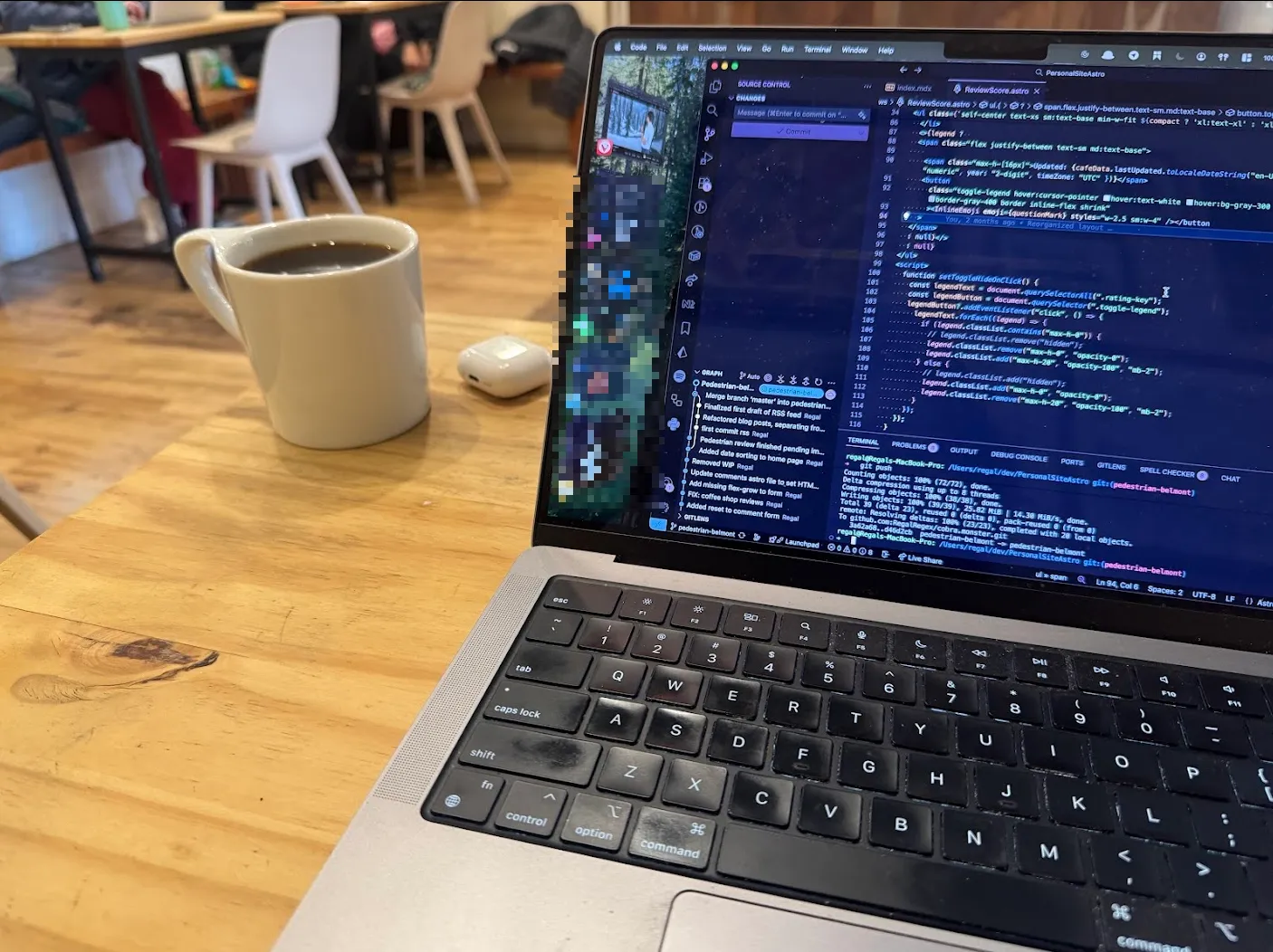 Light wooden table with a macbook open to this website's code base. The focus is on the cup of coffee in far, top-left of the table